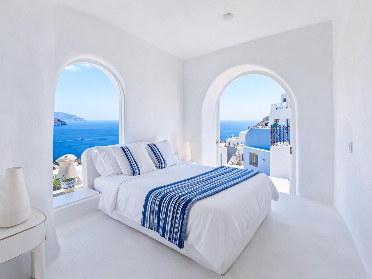 White-washed bedroom with linen bedding and open shutters to the sea